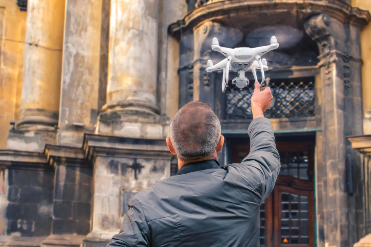A man near a building holds a drone | Skylum Blog