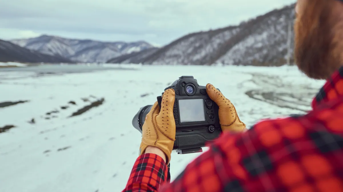 Photographer in gloves holding camera in the mountains| Skylum Blog