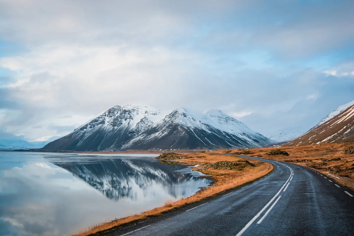 Misty mountains with a road and water in the foreground| Skylum Blog