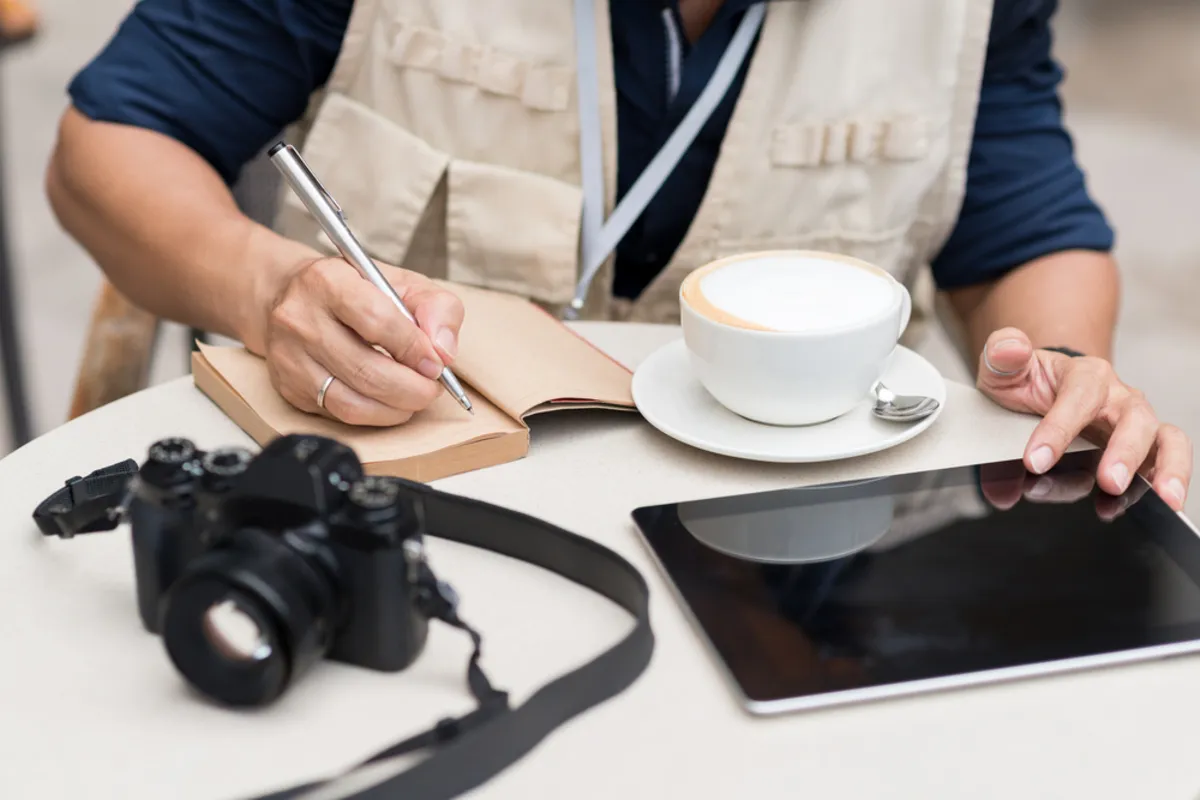 A photographer with camera and laptop takes notes in a notebook | Skylum Blog