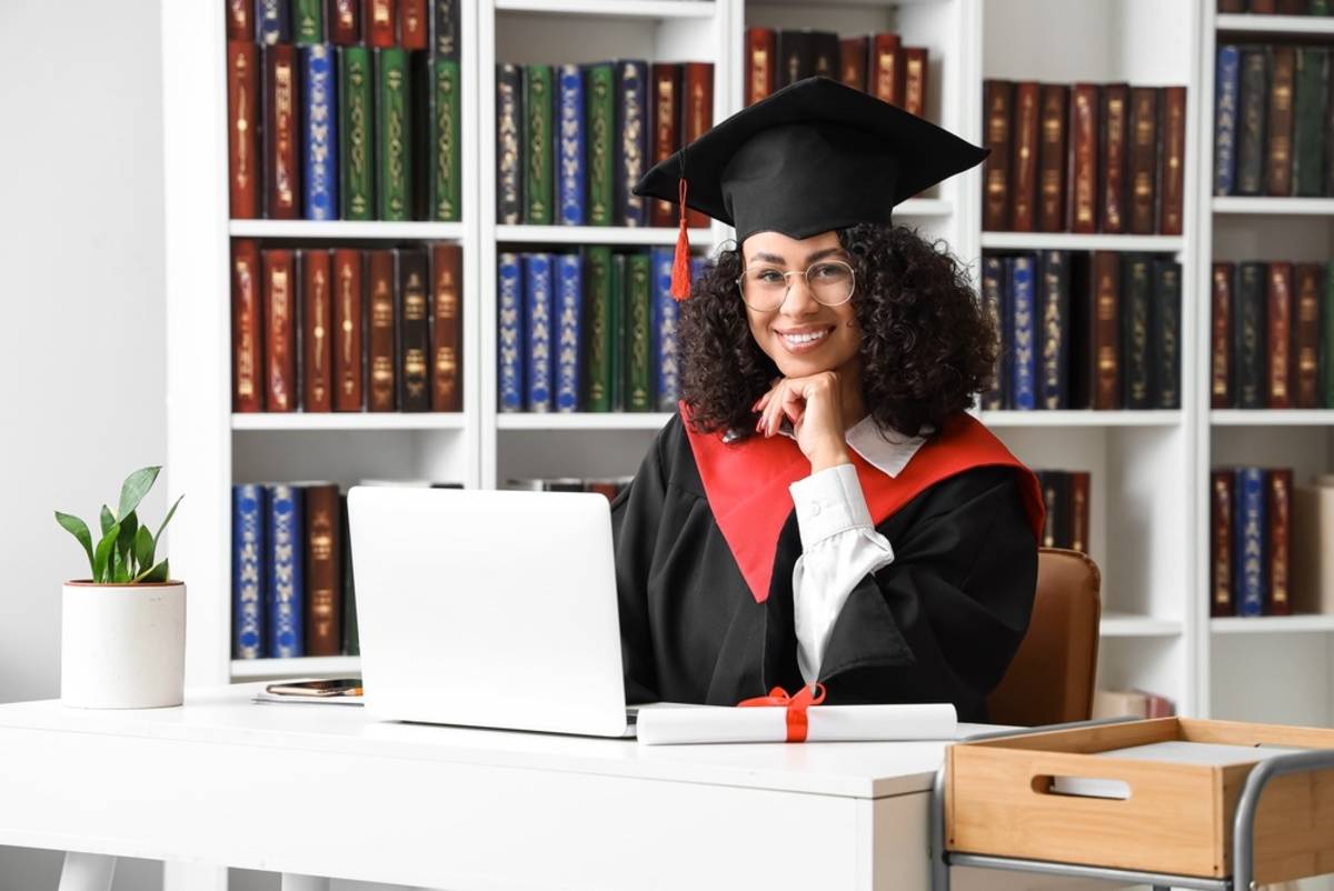 Graduate sitting at a desk in front of bookshelves | Skylum Blog


