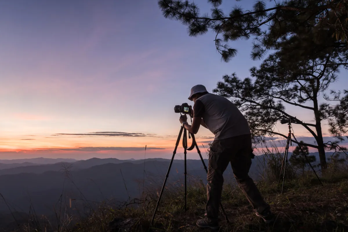 A photographer takes a photo with a camera on a tripod | Skylum Blog