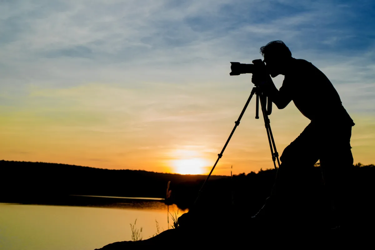 Photographer taking pictures of sunset holding camera on tripod | Skylum Blog