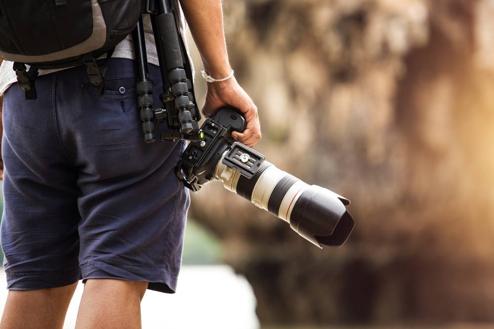 Photographer carrying camera with telephoto lens outdoors | Skylum Blog