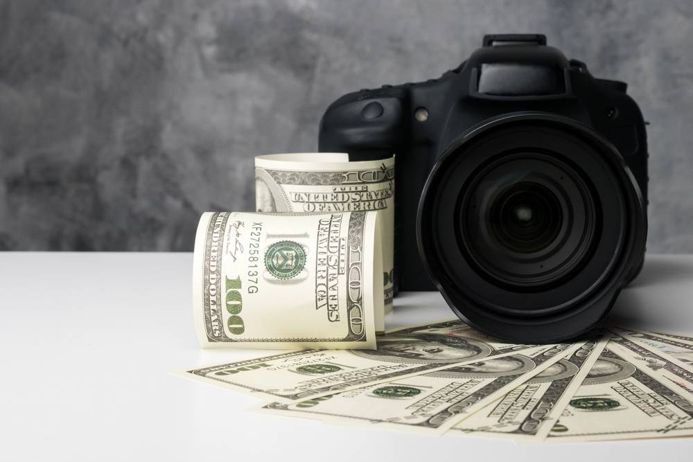 DSLR camera next to dollar banknotes on white desk | Skylum Blog