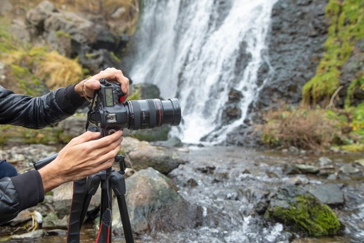 Hands adjusting DSLR camera on tripod by river | Skylum Blog


