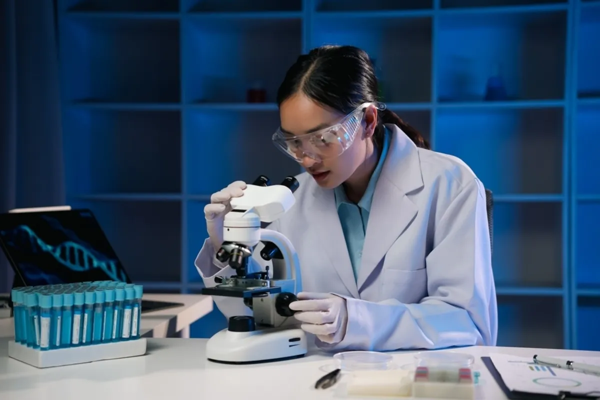 A lab technician looks through a microscope | Skylum Blog