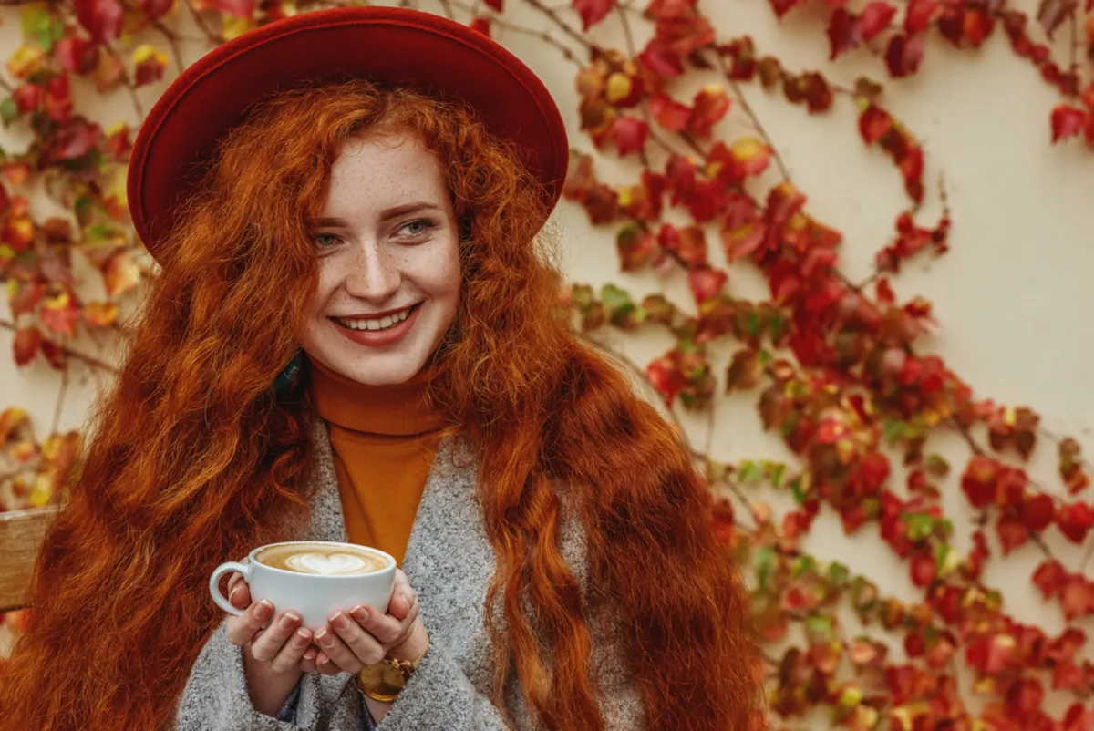 Red-haired girl in a hat holding a cup of coffee in autumn | Skylum Blog