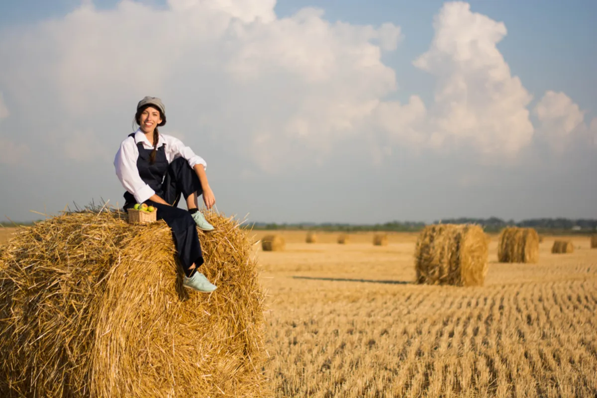 A girl in a hat on a bale of hay in autumn | Skylum Blog