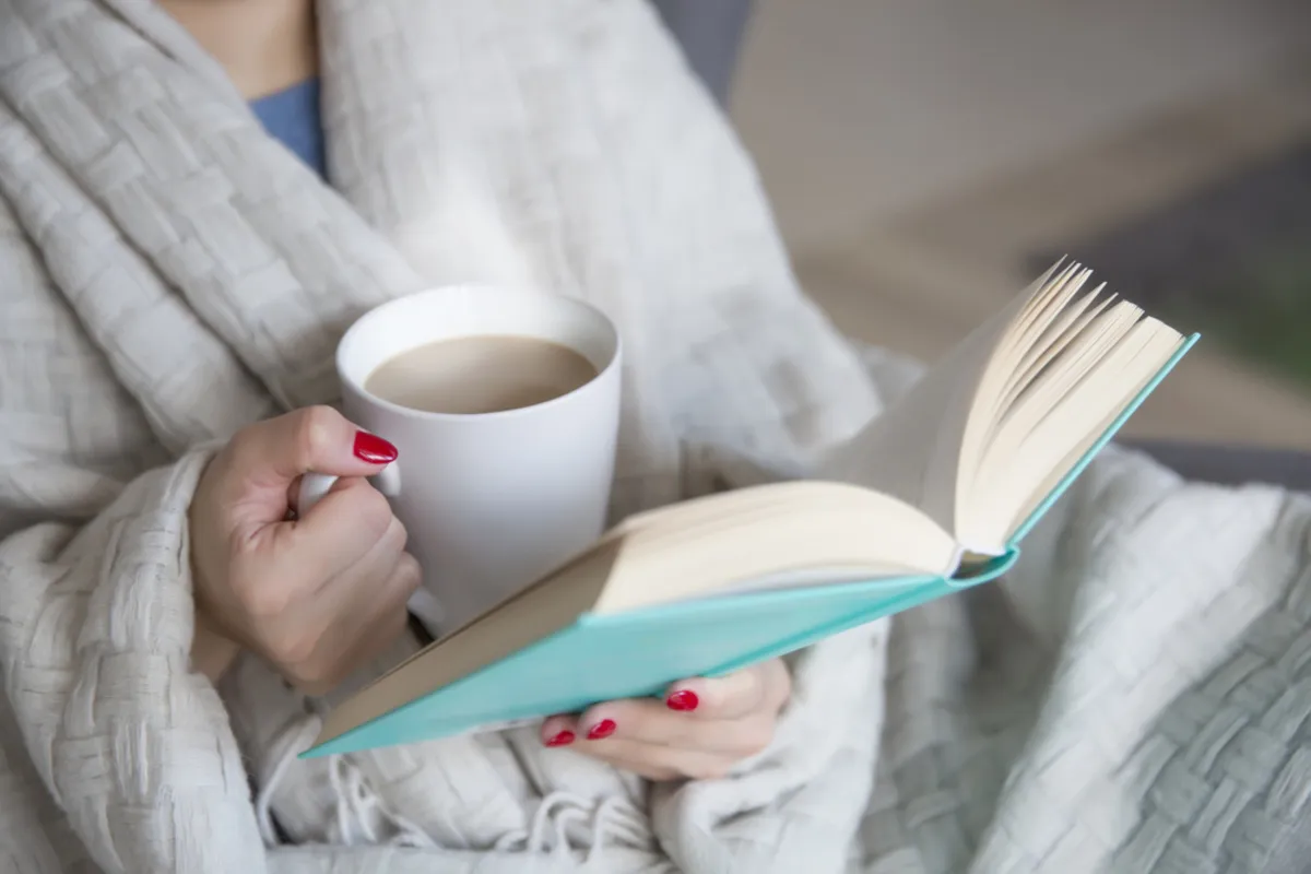 A close-up of a cup of coffee and a book in a girl's hands | Skylum Blog