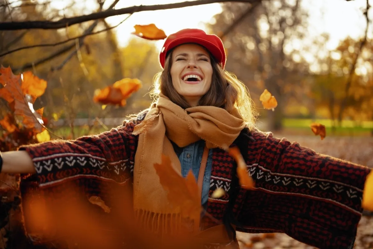 A girl in a hat and scarf scatters autumn leaves | Skylum Blog
