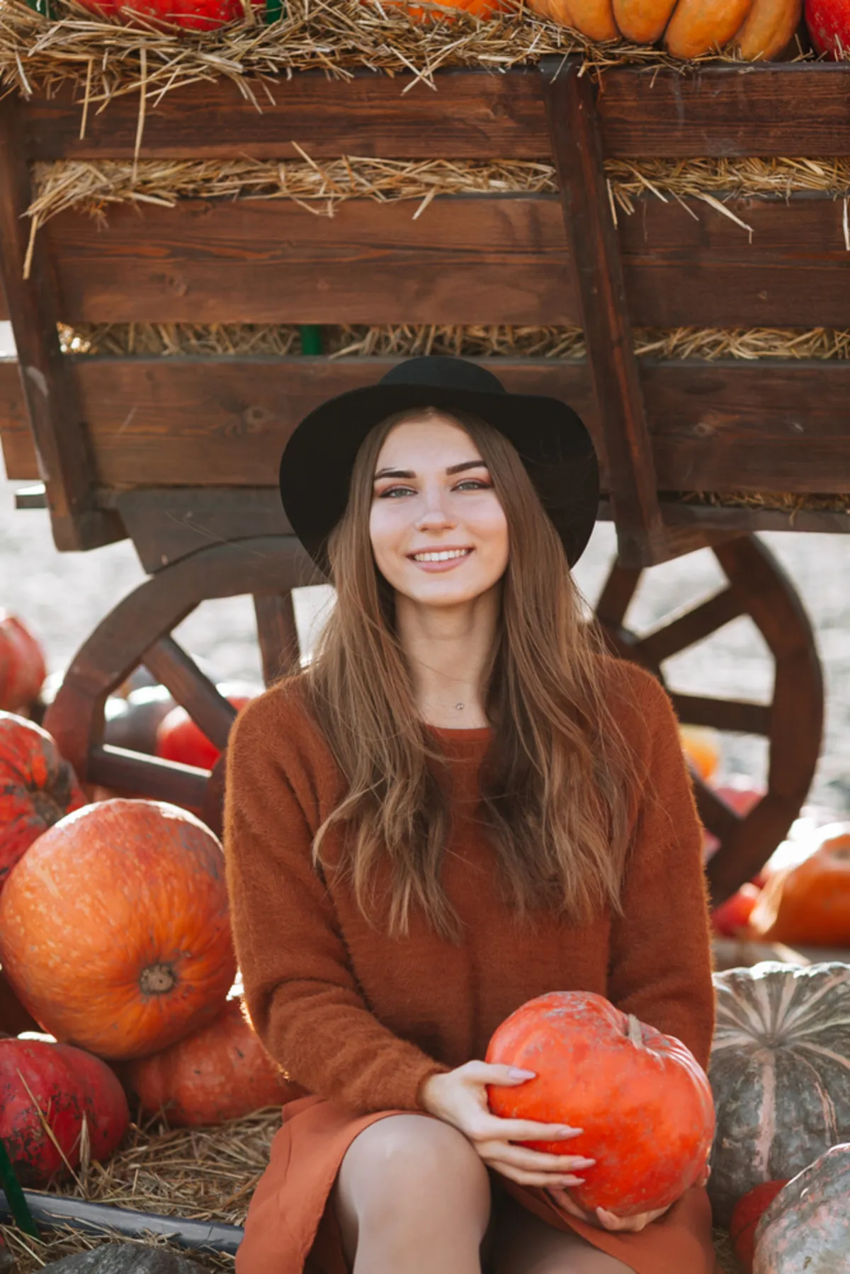 A girl in a black hat holds a pumpkin in her hands | Skylum Blog