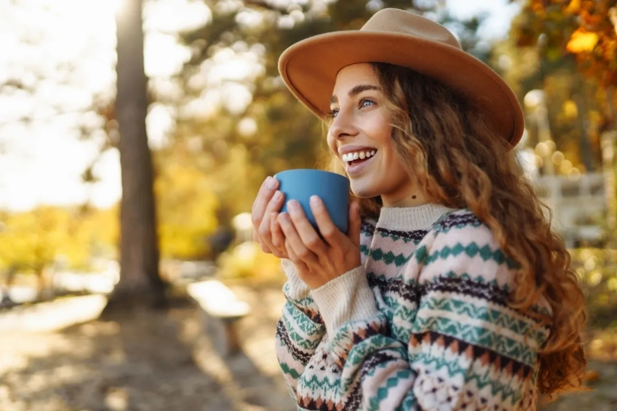 A girl in a hat and a warm sweater holds a cup in her hands | Skylum Blog