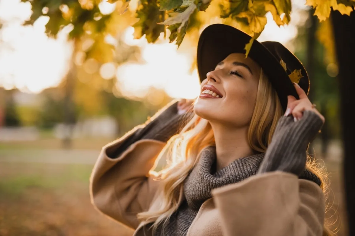 A girl holds a hat in her hands under an autumn tree | Skylum Blog