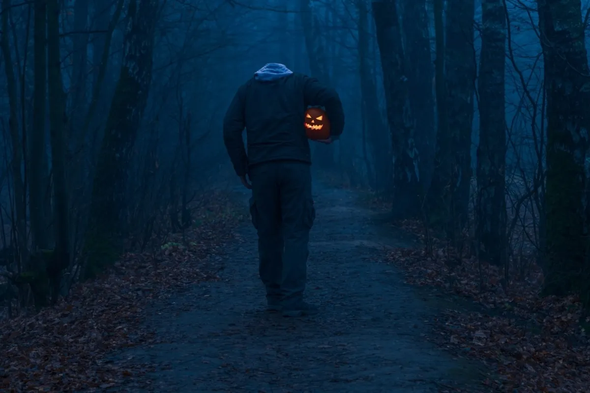 A man with a pumpkin in his hands walks along a dark path | Skylum Blog