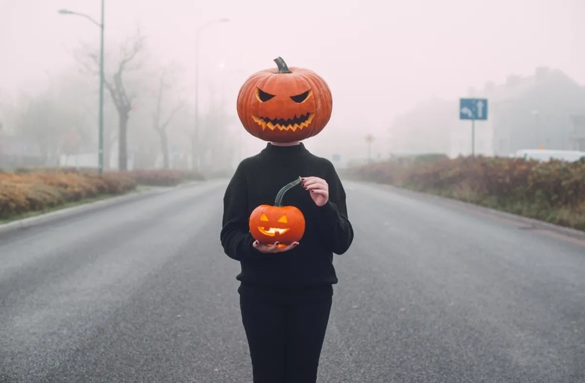 A girl with a pumpkin on her head stands on a foggy road | Skylum Blog