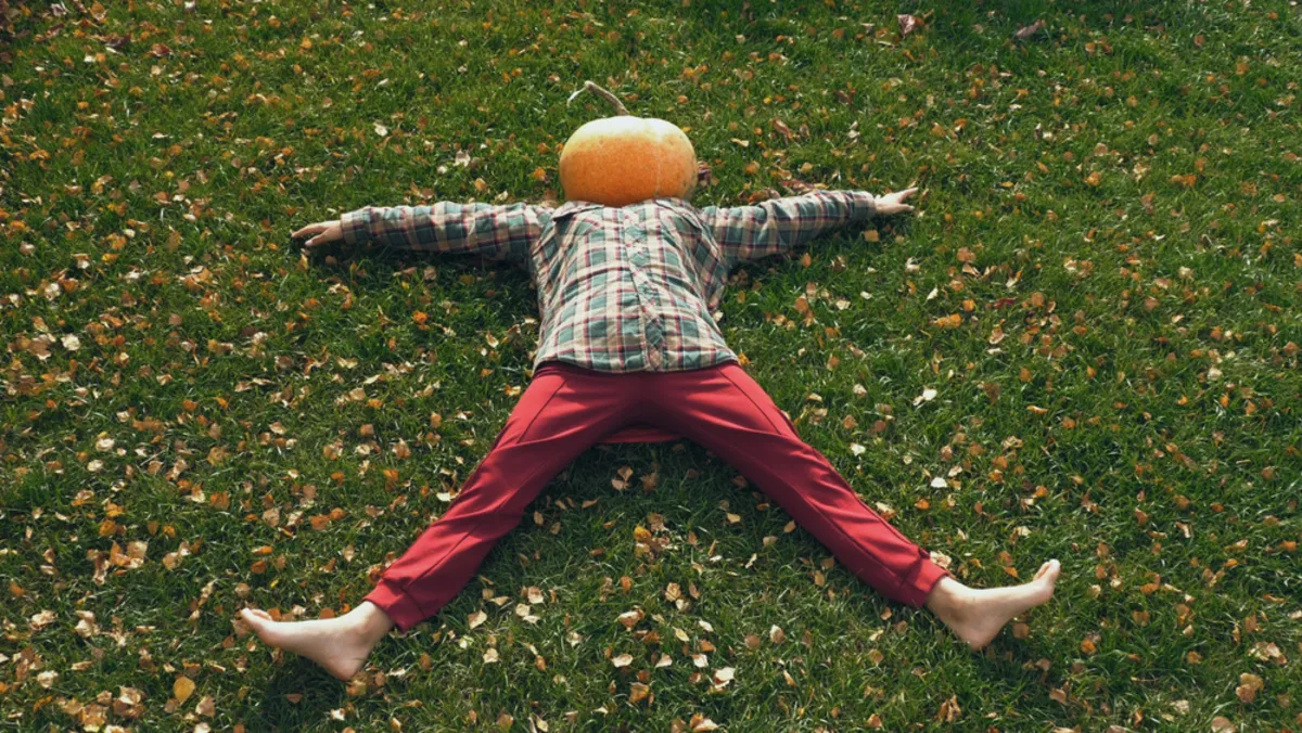 A man with a pumpkin on his head lies on the grass | Skylum Blog