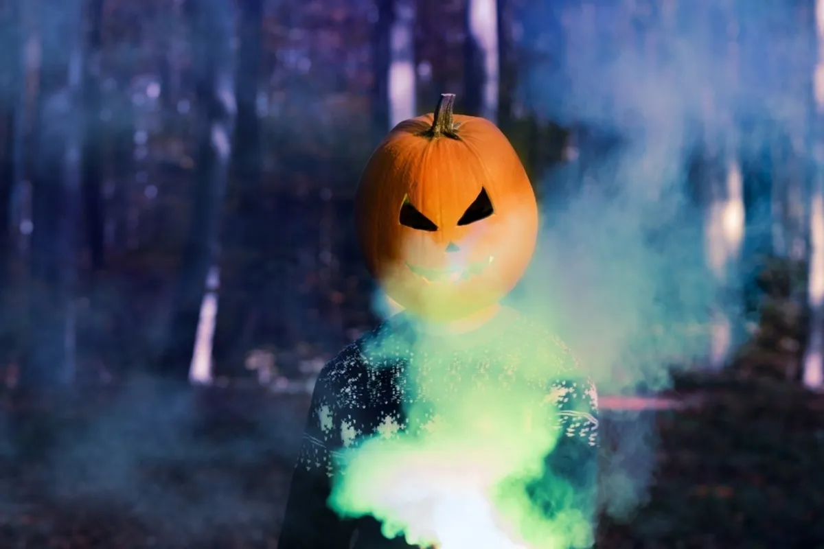A guy with a pumpkin on his head is holding a green smoke bomb | Skylum Blog