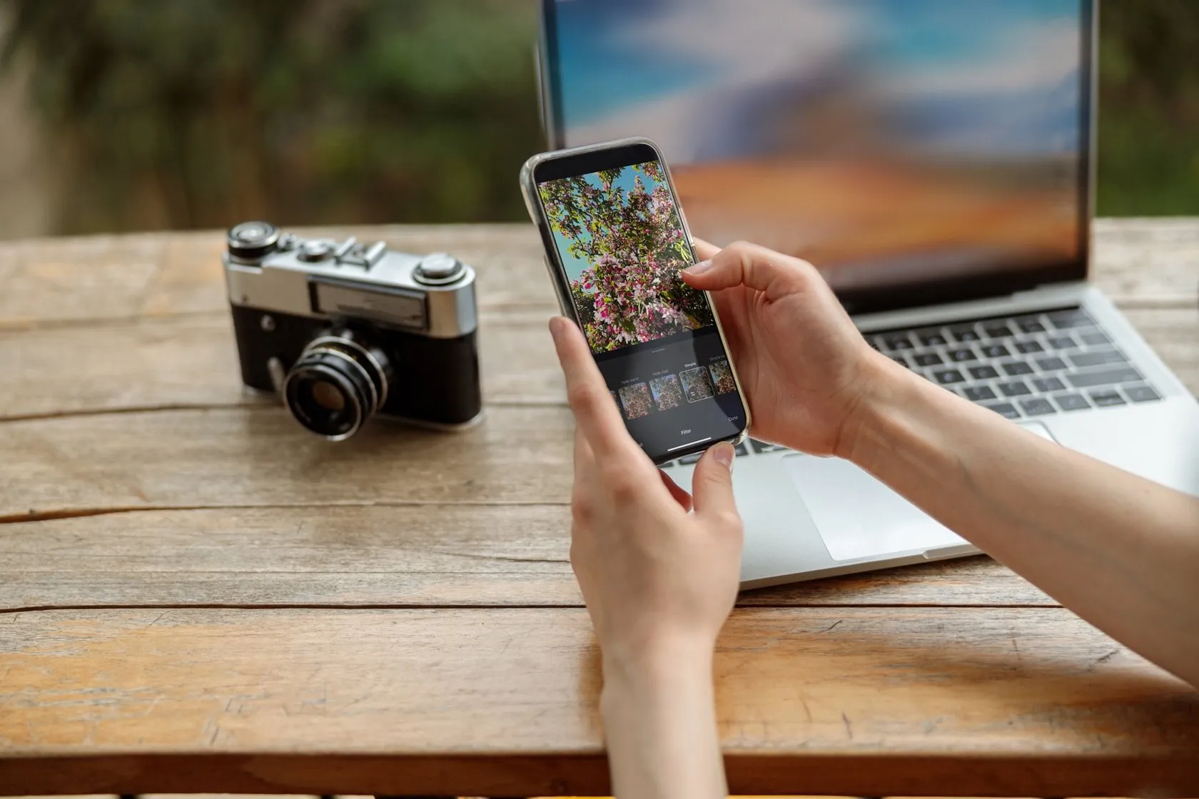 A phone with a photo editor in hand a camera and a laptop nearby | Skylum Blog