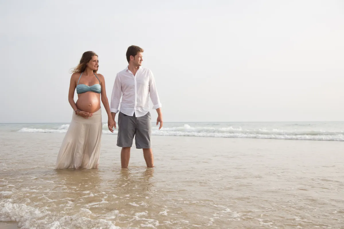 A man and his pregnant wife are walking along the seashore | Skylum Blog