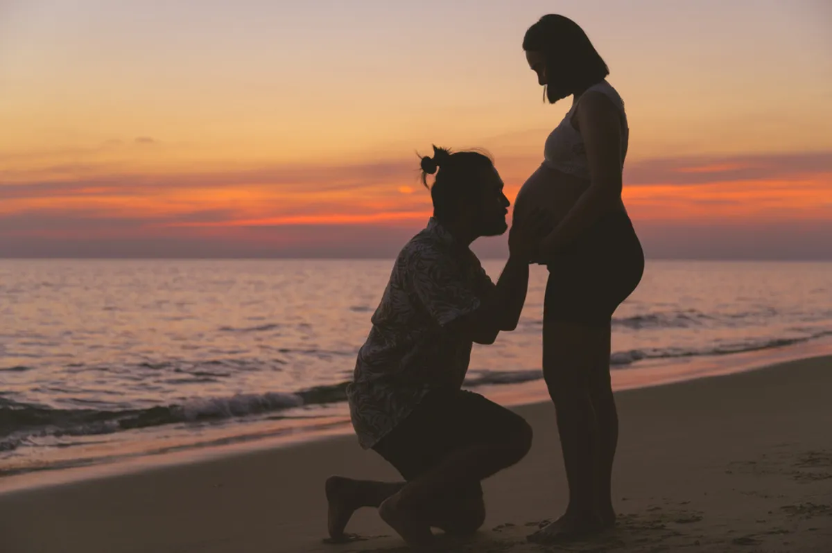 A man kisses his pregnant wife's belly at sunset by the sea | Skylum Blog