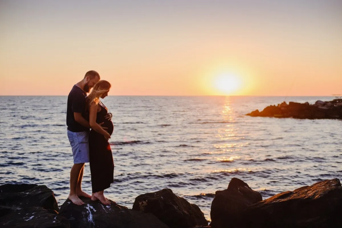A man hugs his pregnant wife at sunset by the sea | Skylum Blog
