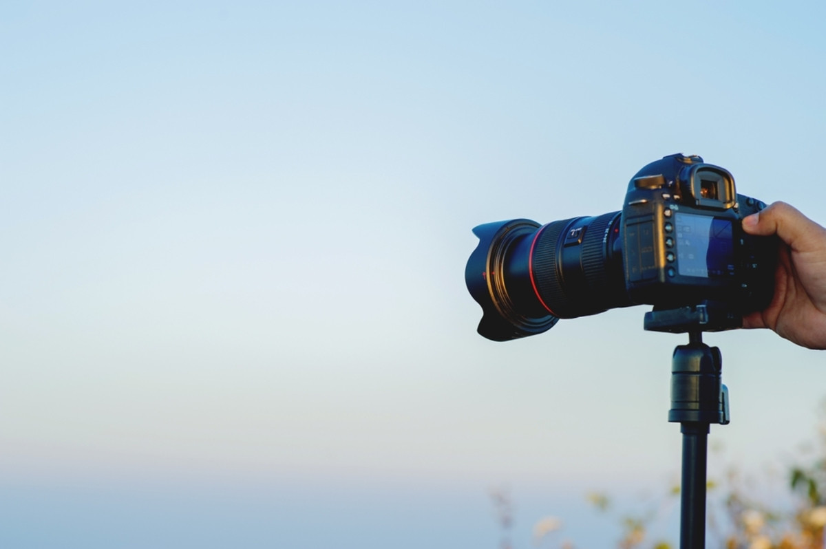 A photographer takes a photo with a camera on a tripod | Skylum Blog
