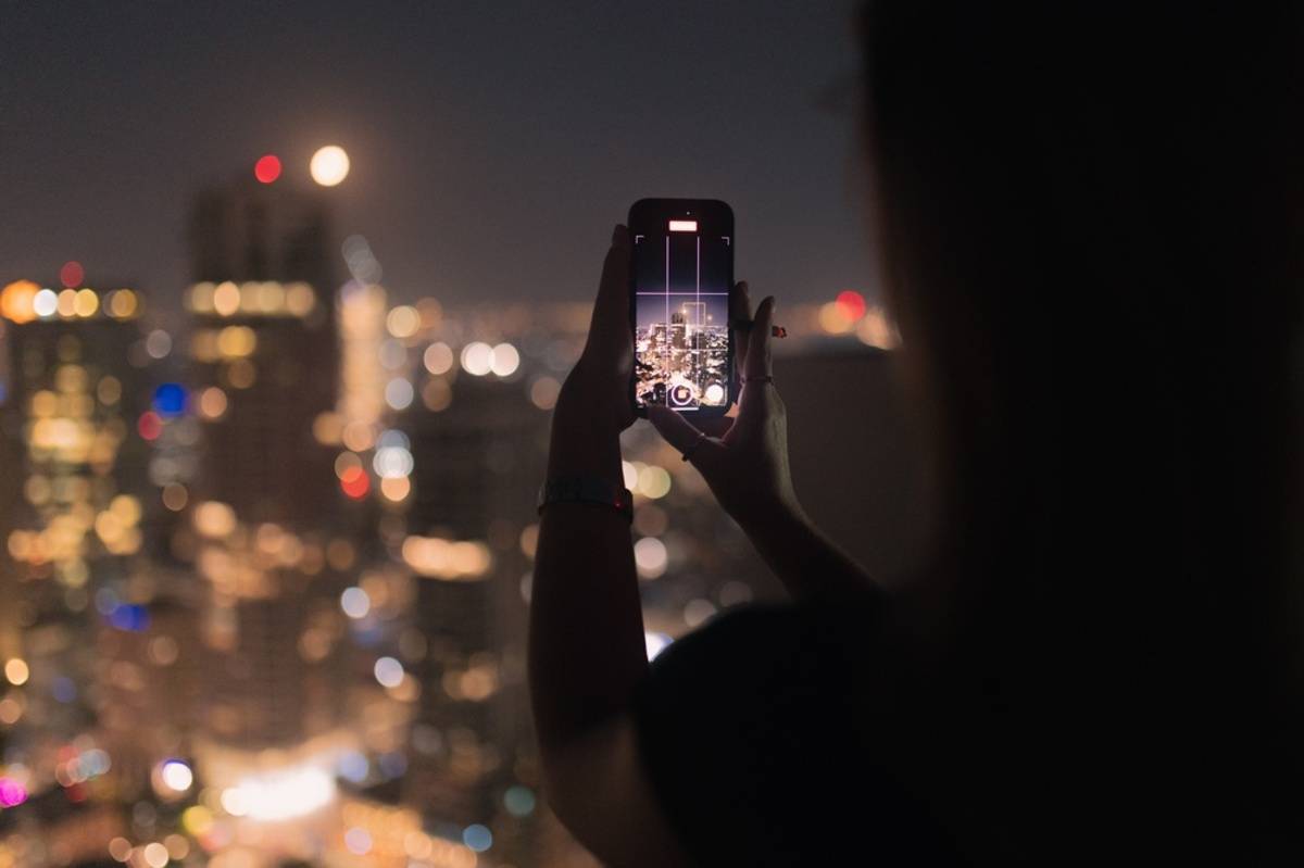 A girl takes a photo of a city at night on her smartphone | Skylum Blog

