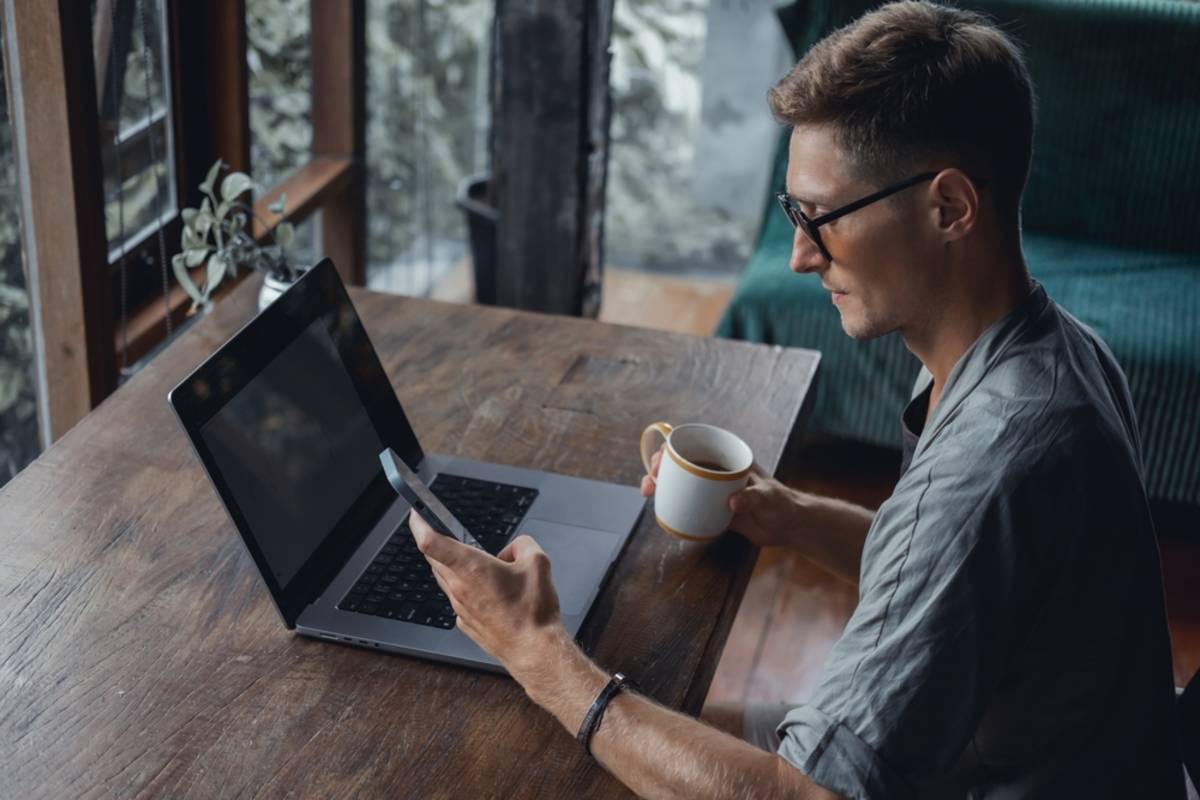 A guy at a laptop with a smartphone in his hands | Skylum Blog

