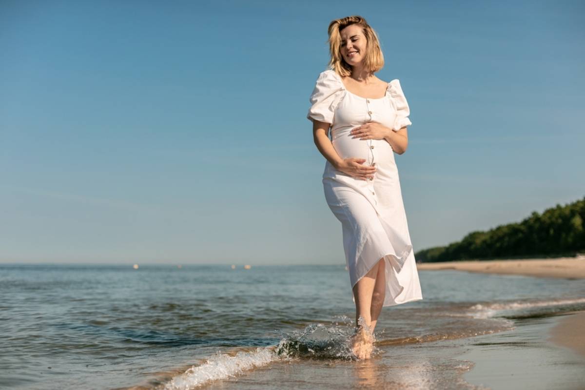 Pregnant woman standing in shallow sea at the beach | Skylum Blog

