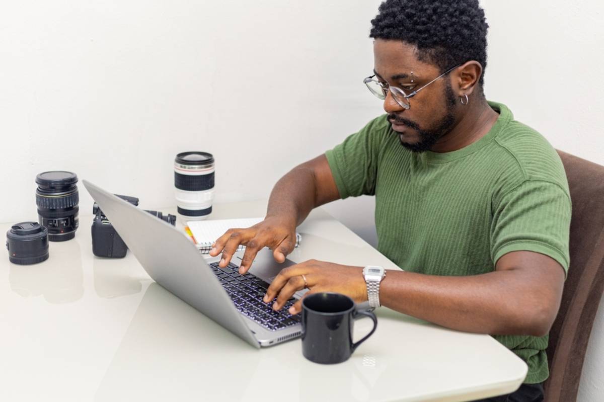 Fotograf, der an einem Laptop mit seiner Kameraausrüstung arbeitet | Skylum-Blog

