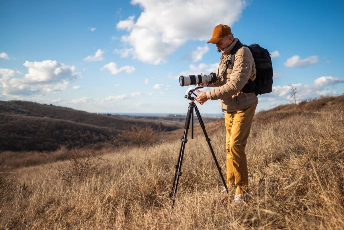 A photographer takes a photo outdoors with a camera on a tripod | Skylum Blog

