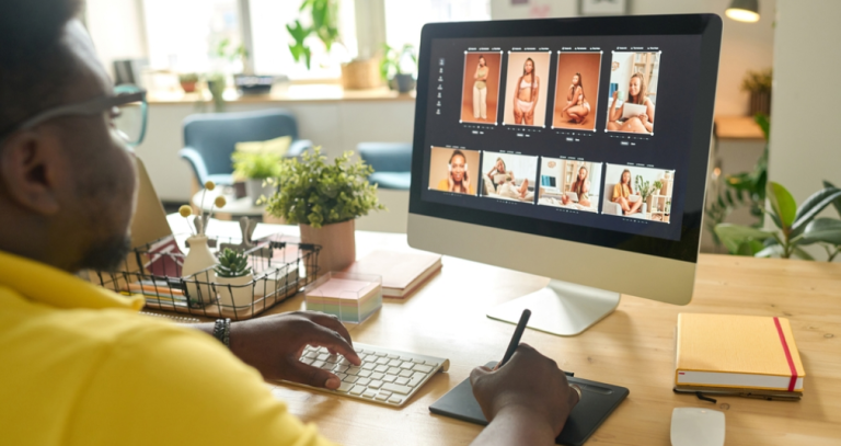 Man at a desk reviewing a grid of portrait photos on a monitor, with keyboard and stylus tablet