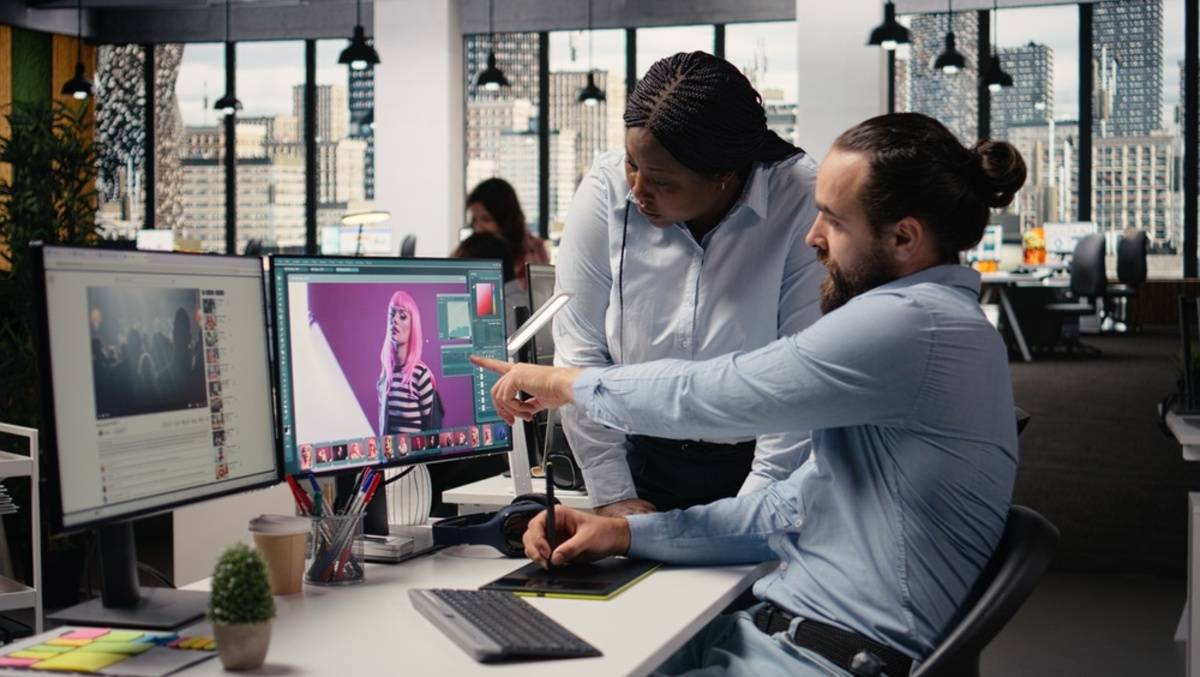 Two editors reviewing a pink-haired portrait on a dual-monitor photo editing workstation