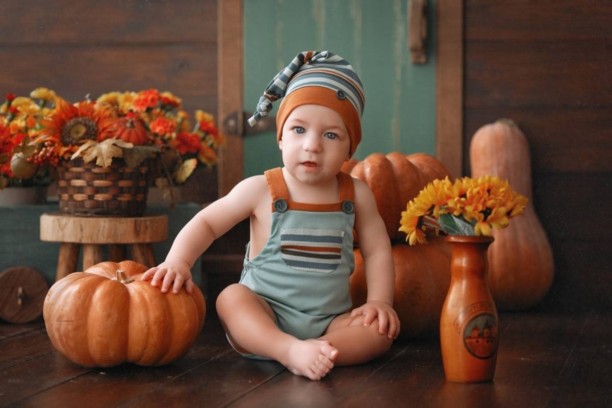 Baby sitting indoors surrounded by pumpkins