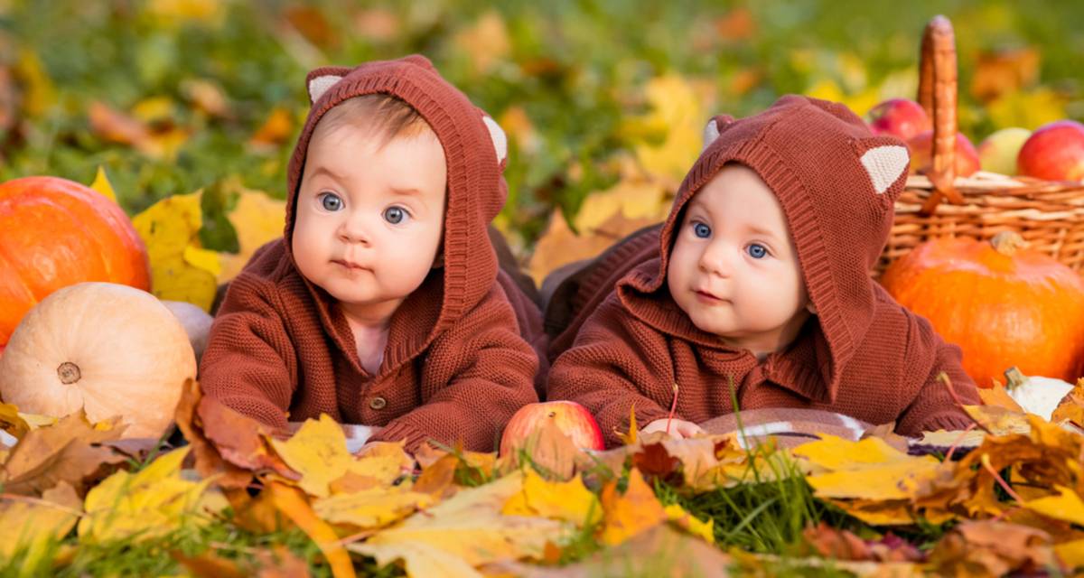 Two babies in bear suits lying in autumn leaves