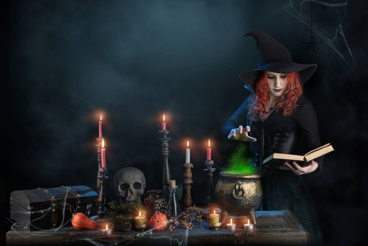Witch in a pointed hat stirs green glowing smoke from a cauldron beside a skull and candles