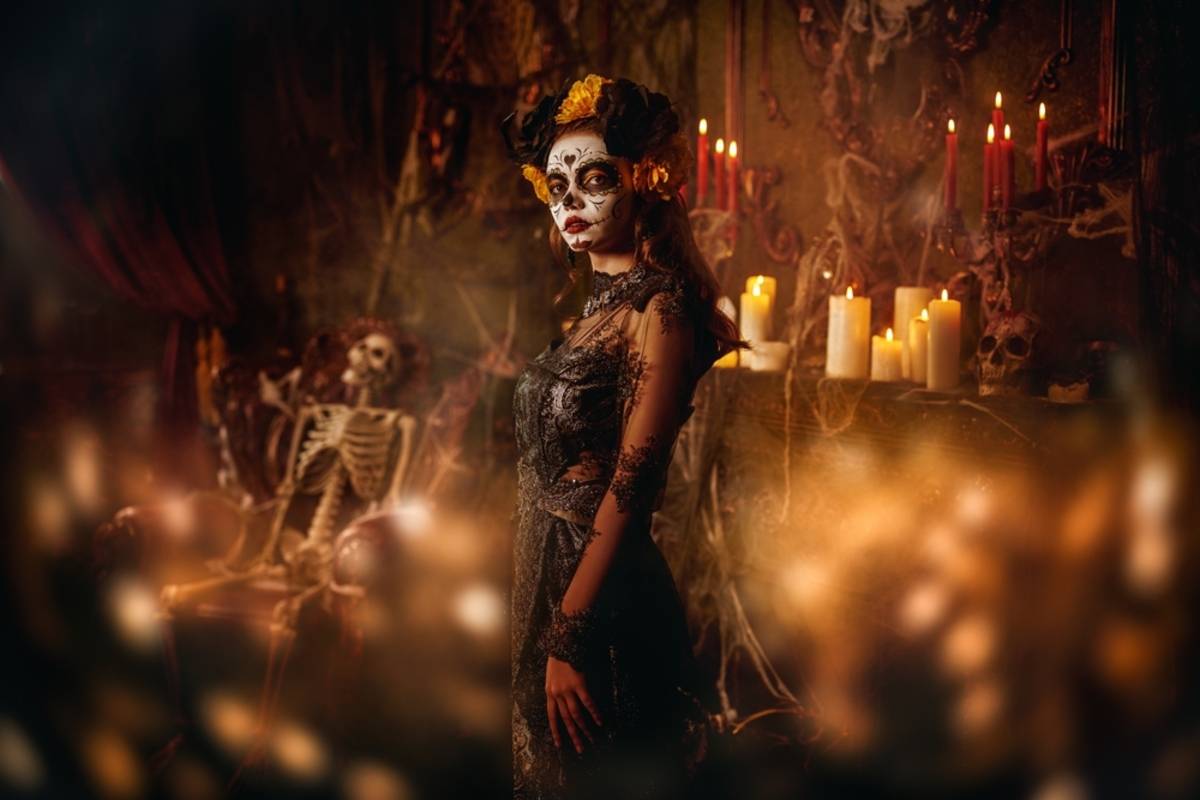 Woman with Day of the Dead face paint and lace dress beside a seated skeleton and lit candles