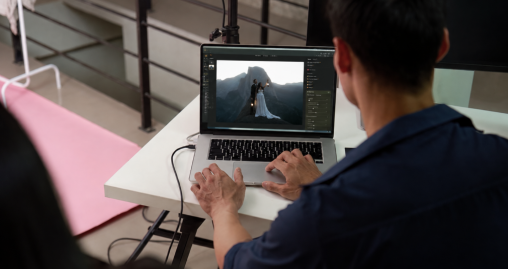 Editor at a laptop with Luminar open on a wedding couple photo against mountains