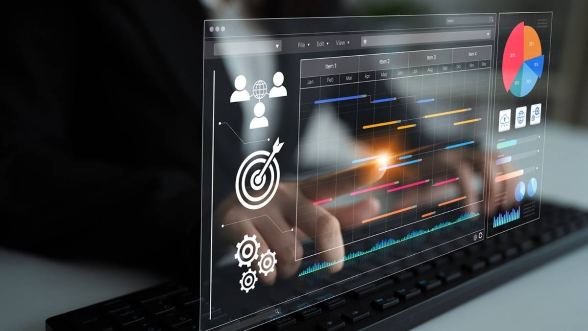 Transparent dashboard overlay with Gantt chart bars, pie chart and icons above a hand typing on a keyboard