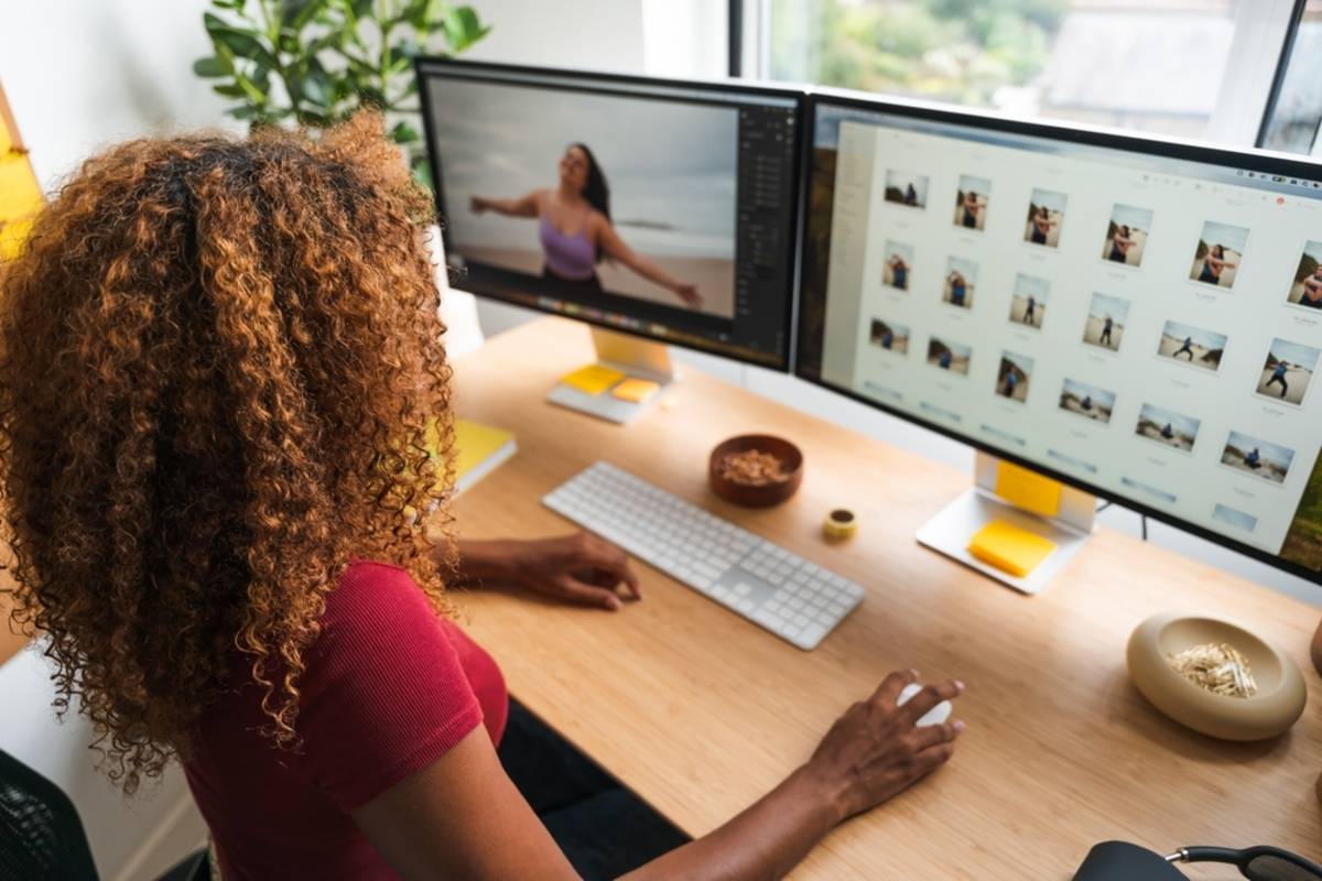 Dual monitors show a beach photo editor and thumbnail grid of similar shots beside a keyboard