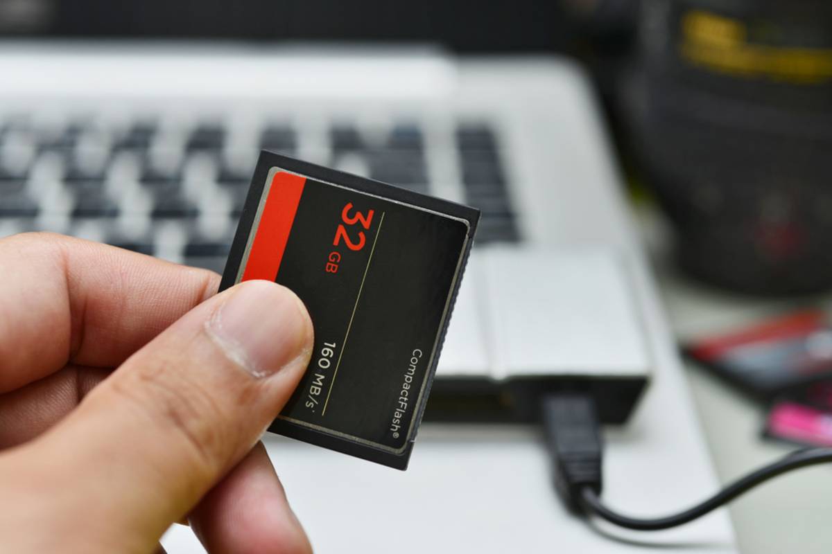 Hand holding a 32GB CompactFlash card over a laptop keyboard and card reader