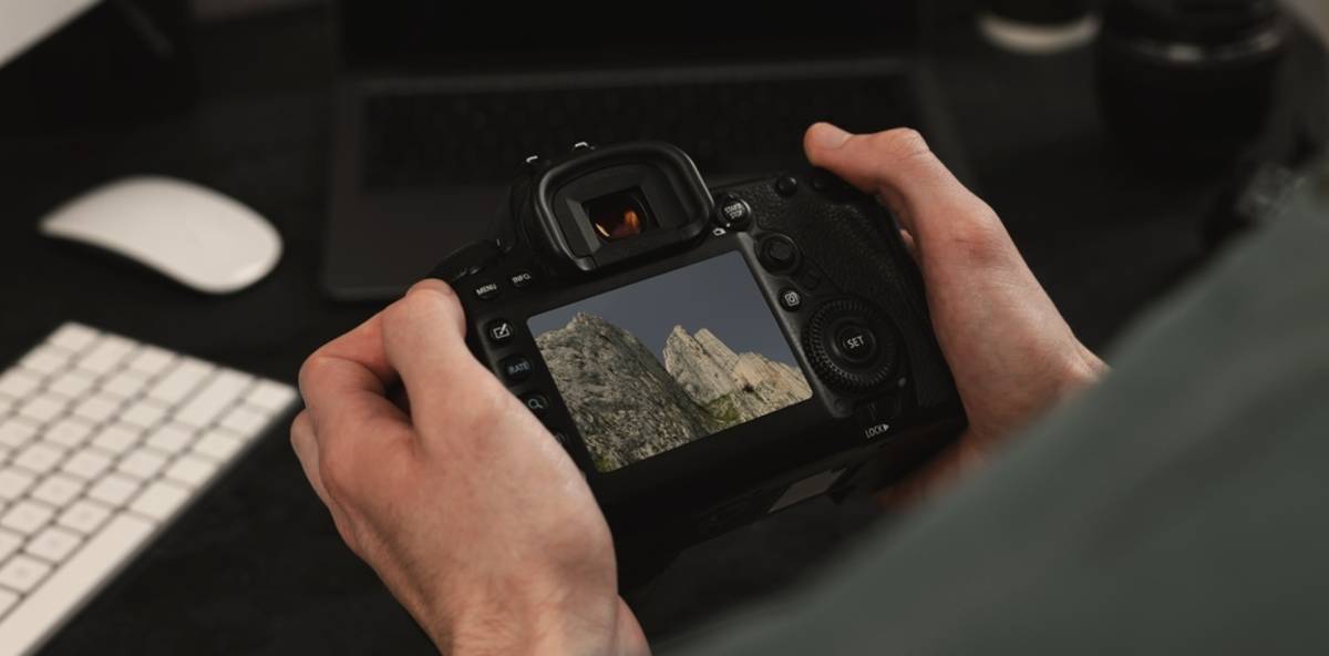 Hands holding a DSLR reviewing a mountain photo on its rear screen at a desk