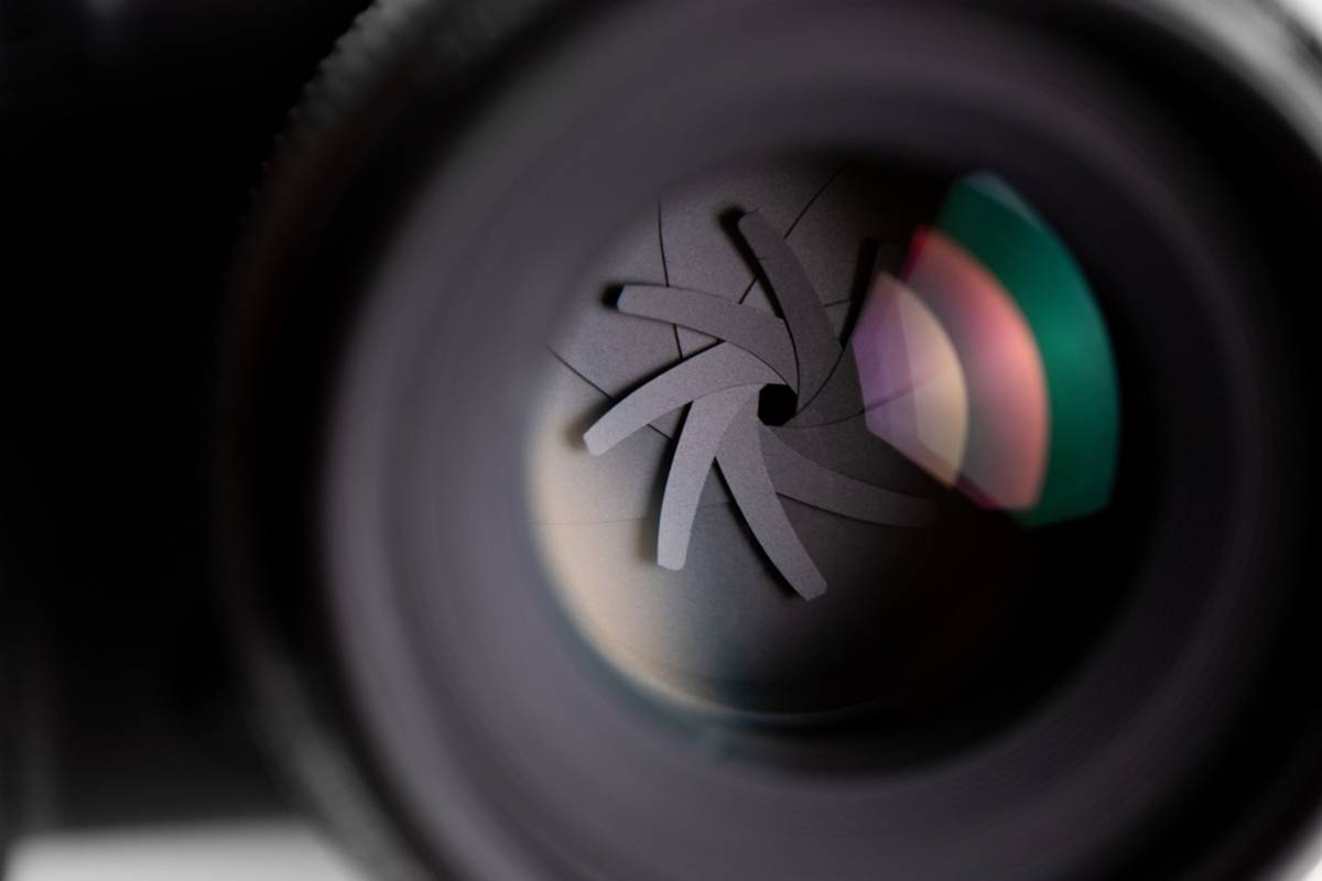 Close-up of a camera lens aperture blades forming a narrow opening with colorful internal reflections