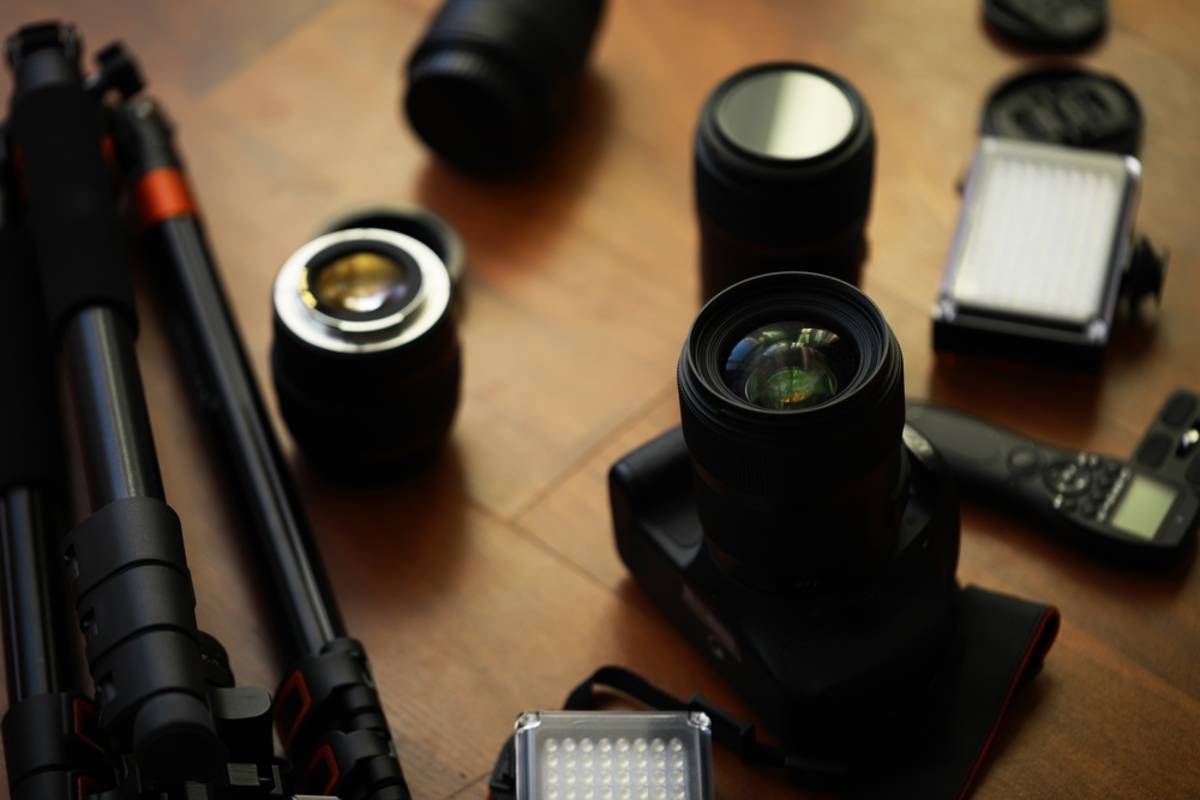 Camera with lens, spare lenses, tripod, LED panels and audio recorder laid out on a wooden desk