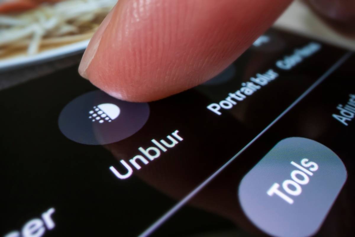 Finger tapping the Unblur icon on a phone screen next to Portrait blur and Tools buttons