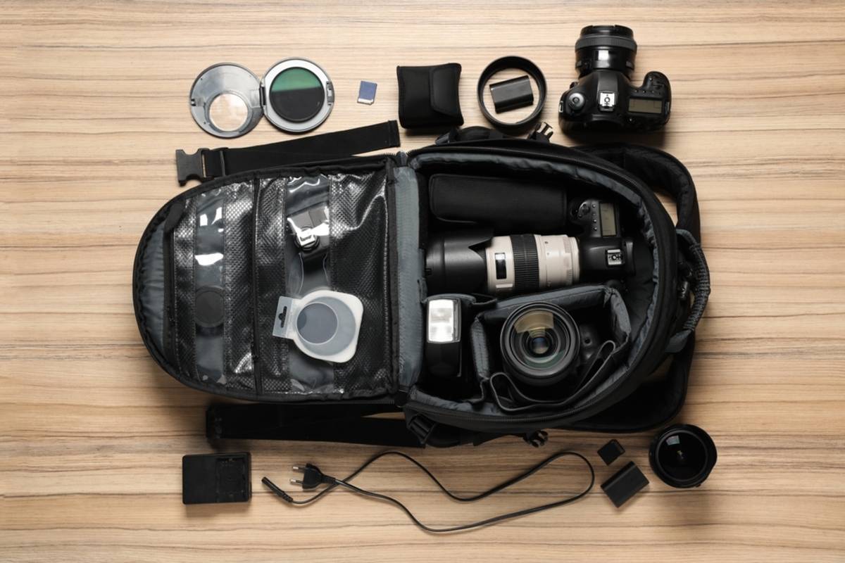 Open camera backpack with lenses, flash, filters, memory cards and cables laid out beside it