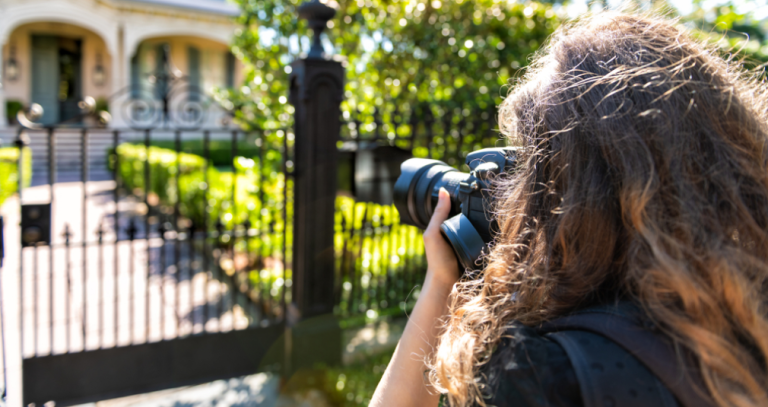 Curly-haired woman photographing a wrought iron gate and house with a camera